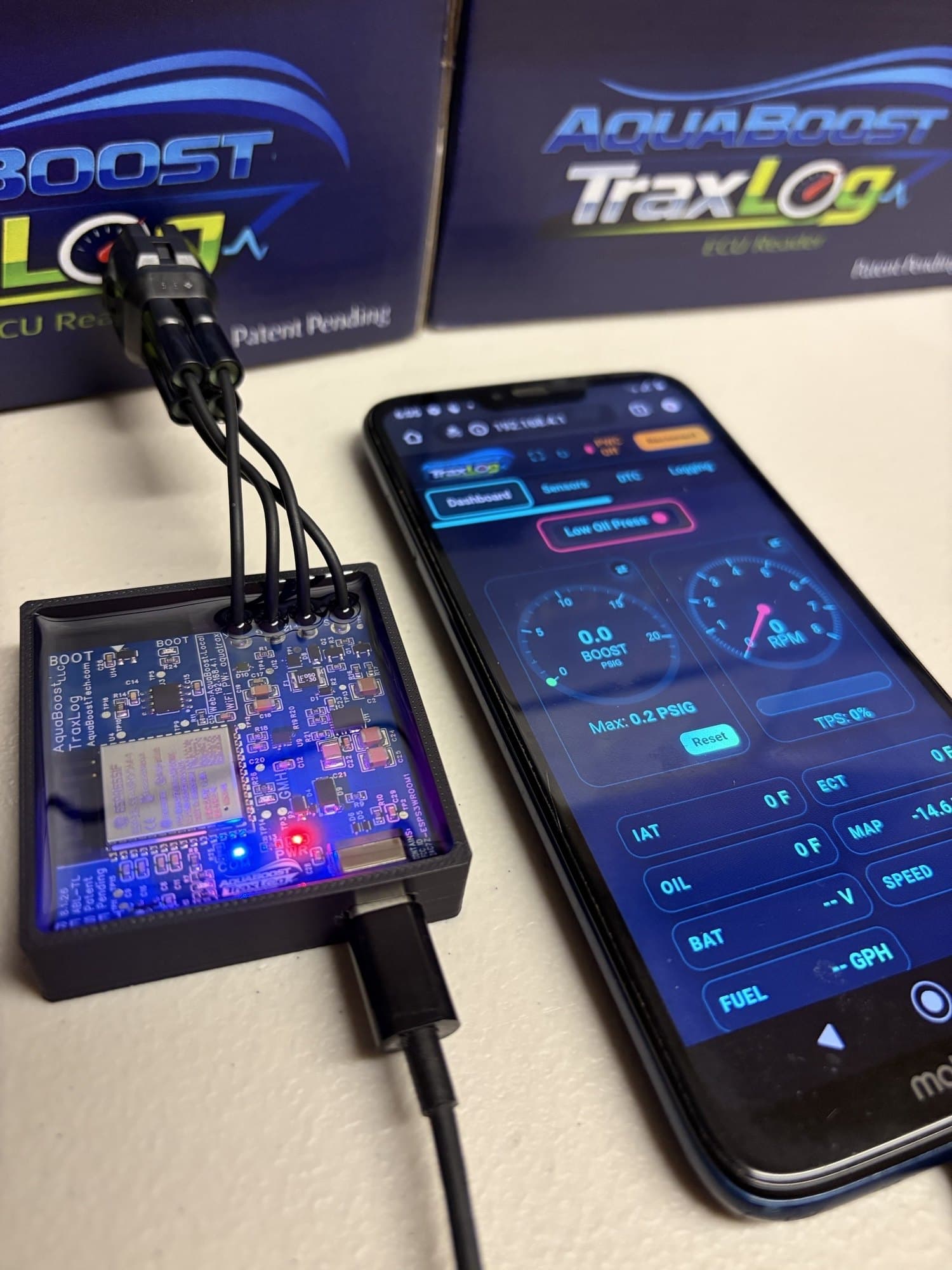 An AquaBoost TraxLog module powered up, next to a phone showing the live dashboard